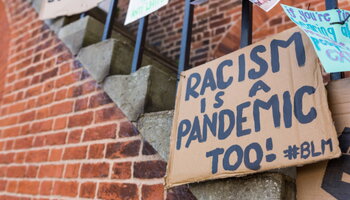 cardboard protest signs, including one reading Racism is a pandemic too, affixed to a stairway