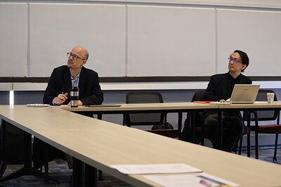 Illinois professor Matthew Winters and OMU professor Hisatsugu Kusabu seated at a conference table.